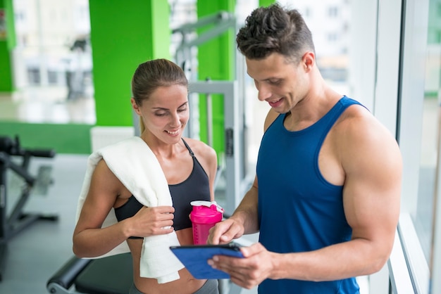 Die Frau diskutiert mit einem Fitnesstrainer mit einem Tablet