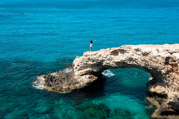 Die Frau freut sich auf dem Felsen am Meer Eine Frau am Rand einer Klippe am Meer