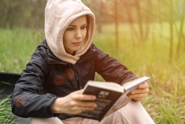 Die Frau hält ein Buch in den Händen. Lesen im Park, im Wald. Ruhe, Training, Entspannungskonzept.