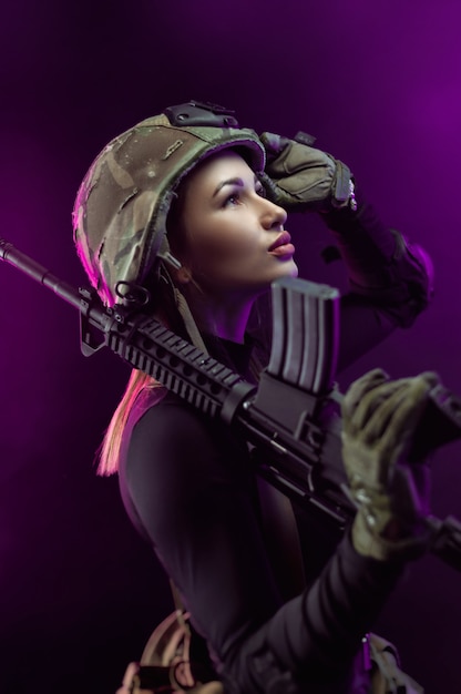 Die Frau in einer militärischen Airsoft-Uniform mit einem amerikanischen automatischen Gewehr und einem Helm auf dunklem Hintergrund