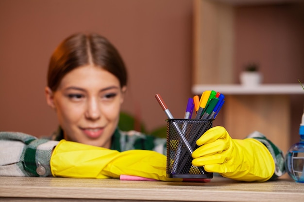 Die Frau reinigt das Büro in den gelben Handschuhen und wischt den Staub vom Schreibtisch