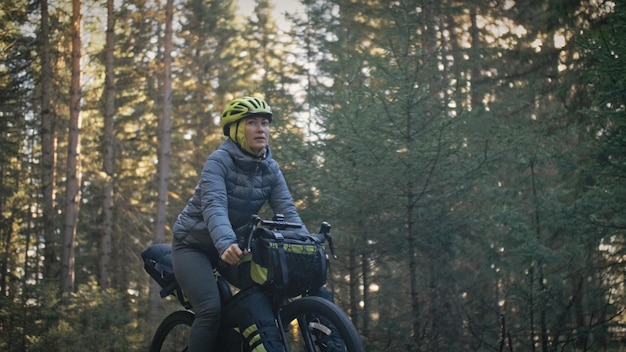 Die Frau reist auf gemischtem Gelände Radtouren mit dem Fahrrad Bikepacking im Freien Die Reise des Reisenden mit Fahrradtaschen Stilvolle Bikepacking-Bike-Sportbekleidung in grün-schwarzen Farben Magischer Waldpark