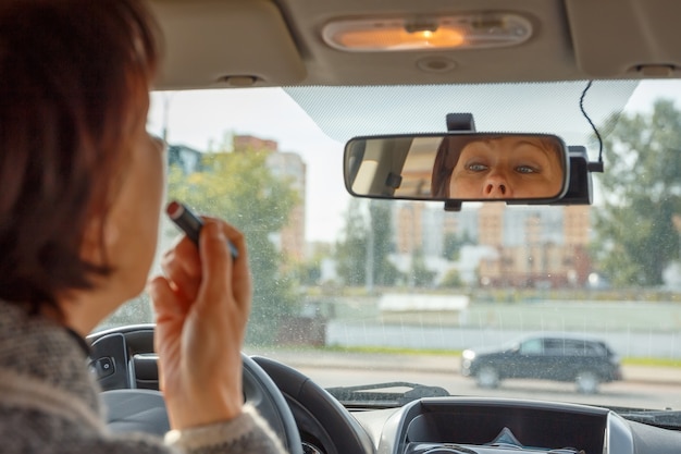 Die Frau schaut in den Rückspiegel des Autos und malt sich die Lippen