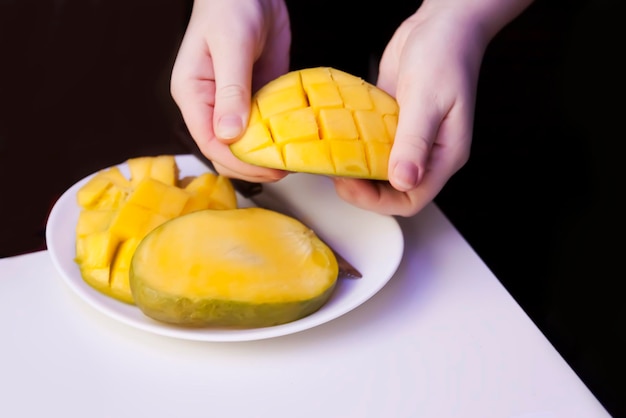 Die Frau schneidet die Mango in Würfel, damit sich das Fruchtfleisch mit einem Küchenmesser leicht von der Schale lösen lässt