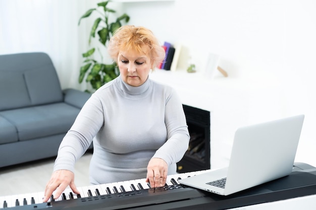 Die Frau spielt den Synthesizer und schaut auf den Laptopbildschirm. Nahaufnahme der weiblichen Hände auf dem E-Piano.