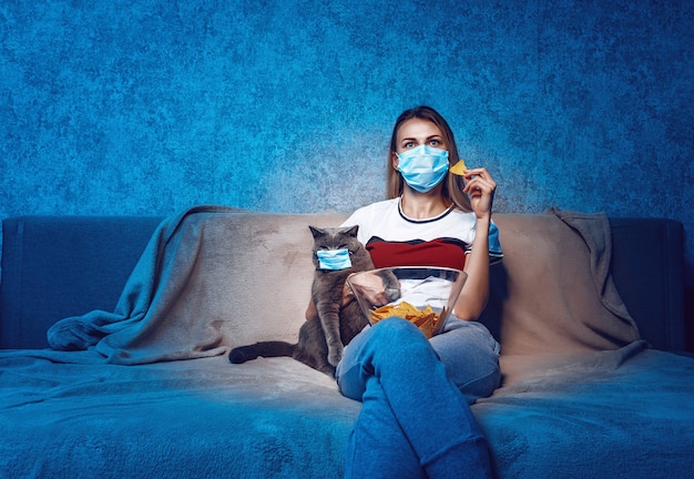 Die Frau und die Katze auf der Couch vor dem Fernseher tragen medizinische Schutzmasken