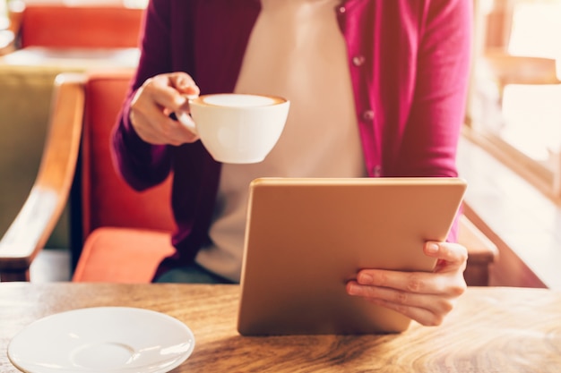 Die Frauenhände, die Computertablette in der Kaffeestube mit Weinlese verwenden und halten, tonten.