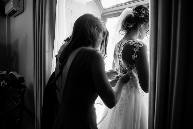 Die Freundin der Braut hilft ihr morgens, sich in ein weißes Hochzeitskleid zu kleiden. Hochzeitsmorgen
