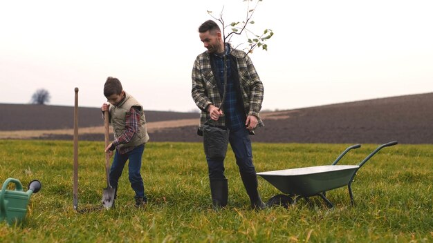 Die freundliche Familie pflanzt einen Baum auf der grünen Wiese