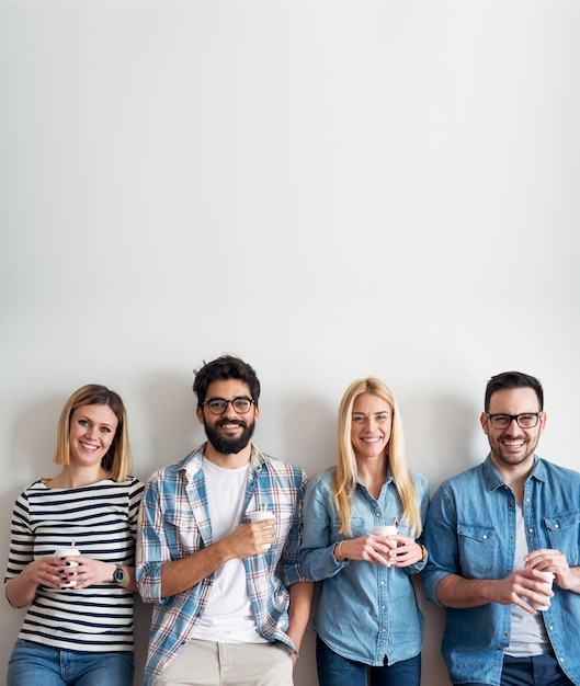 Die fröhliche junge Gruppe von Entwicklern macht draußen eine Kaffeepause, während sie sich an die Wand lehnt.