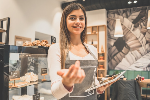 Die fröhliche Kellnerin hält ein Tablet in der Nähe der Vitrine