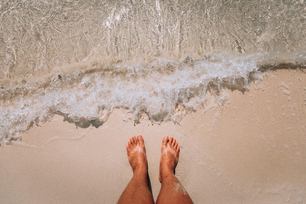 Die Füße der Frau stehen in der Nähe der Meereswellen am rosafarbenen Strand