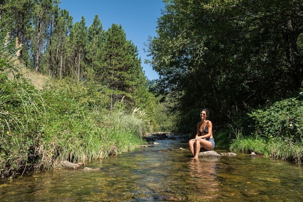 Die ganze Länge der Frau sitzt am Bach im Wald