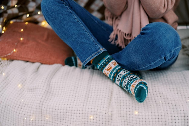 Foto die gekreuzten beine eines mädchens sitzen in socken auf einer decke mit leuchtenden girlanden, die gesichtslos geschnitten sind