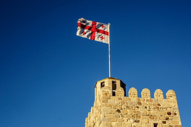 Die Georgia-Flagge auf dem Dach eines alten Turms gegen den klaren blauen Himmel