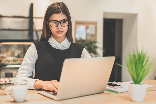 Die Geschäftsfrau mit Brille arbeitet mit einem Laptop