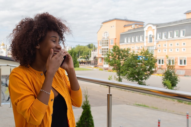 Die glückliche Afroamerikanerin, die auf der Straße am Telefon spricht