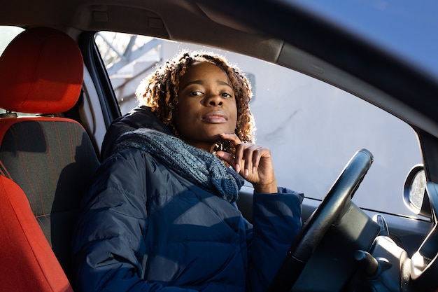 Die glückliche afroamerikanische Frau im Auto, die in die Kamera schaut