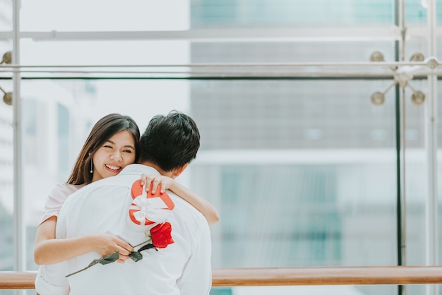 Die glückliche asiatische Frau, die ihren Freund umfaßt, empfangen Valentinsgrußgeschenk