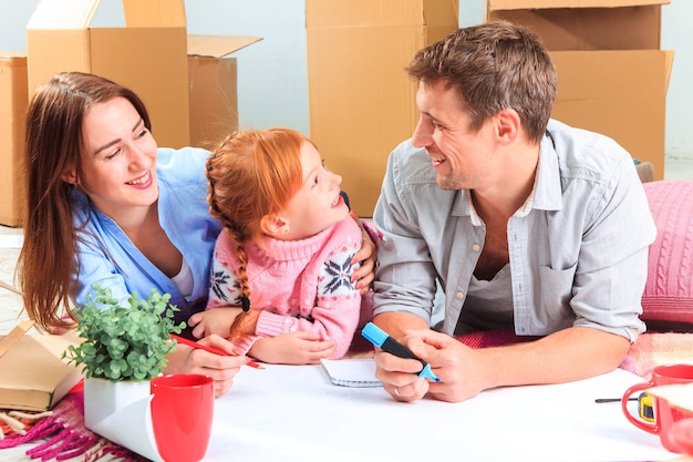 Die glückliche Familie bei Reparatur und Umzug. Die Familie, die eine Unterkunft vor dem Hintergrund von Kisten plant