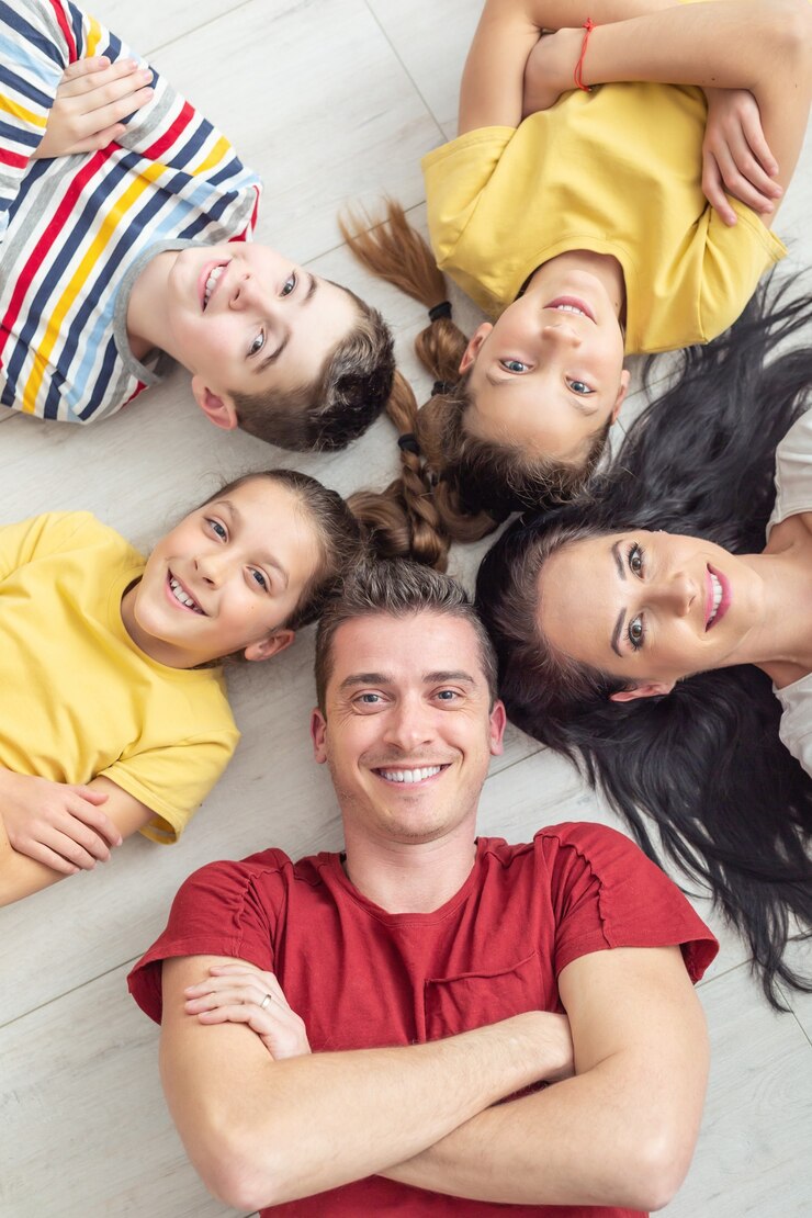 Die glückliche Familie, die auf dem Boden liegt, lächelt und schaut zur Kamera auf.