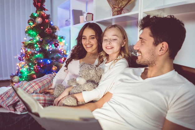 Die glückliche Familie lag auf dem Bett und las neben dem Weihnachtsbaum eine Geschichte