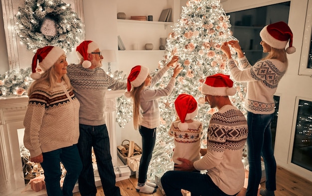 Die glückliche Familie mit rotem Hut schmückt den Weihnachtsbaum