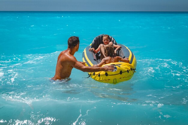 Die glückliche Familie schwimmt während der Sommerferien im gelben Kajak im tropischen Meerwasser. Der Vater bewacht Kinder, die in einem Schlauchboot fahren.