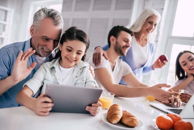 Die glückliche Familie sitzt mit Laptop und Tablet am Tisch