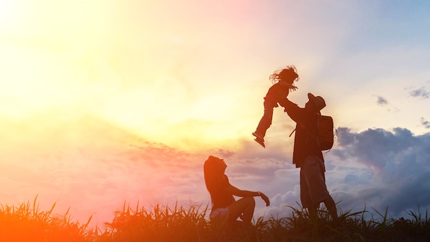 Die glückliche familie von drei leuten, von mutter, von vater und von kind vor einem sonnenunterganghimmel.