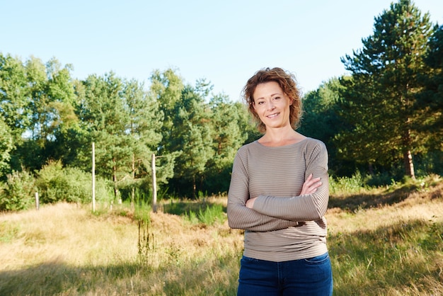 Die glückliche Frau, die mit den Armen steht, kreuzte im Park