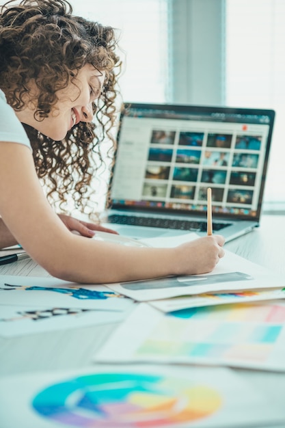 Die glückliche Frau malt ein Bild neben dem Laptop