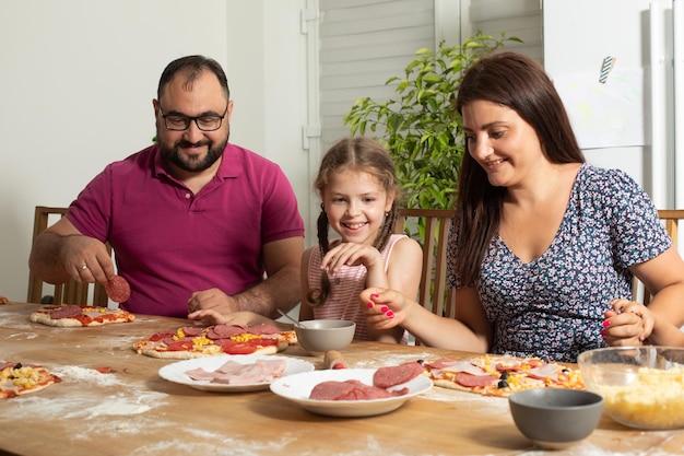 Die glückliche junge Familie kocht hausgemachte Pizza