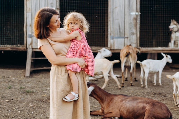 Die glückliche Mutter und ihre Tochter verbringen Zeit auf einer Öko-Farm unter Ziegen.