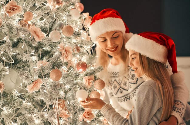 Die glückliche Mutter und Tochter schmücken den Weihnachtsbaum