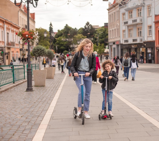 Die glückliche Mutter und Tochter stehen mit Rollern in der Stadt