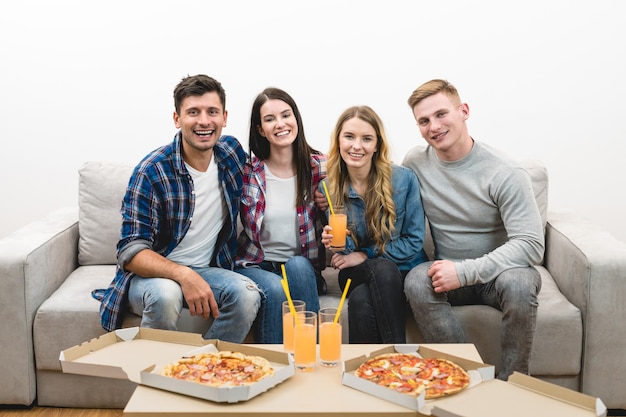 Die glücklichen Freunde mit Pizza und Getränken sitzen auf dem weißen Hintergrund