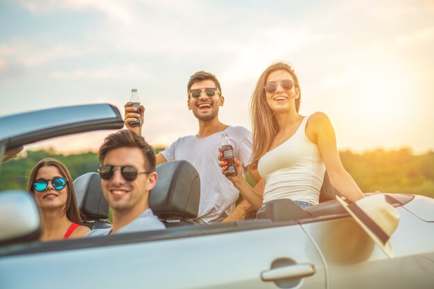 Die glücklichen Freunde sitzen in einem Cabrio vor dem sonnigen Hintergrund