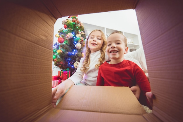 Die glücklichen Kinder öffnen die Kiste neben dem Weihnachtsbaum