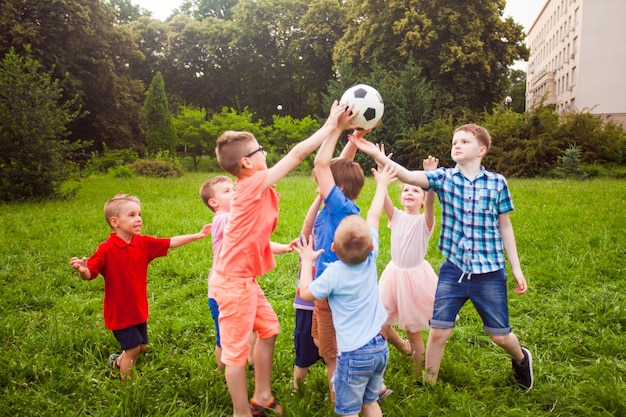 Die glücklichen kleinen Jungen und Mädchen spielen beim Aufheben des Balls