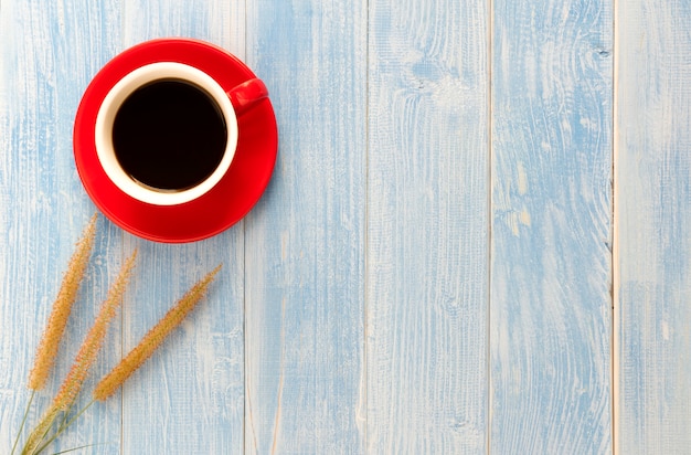 Die Grasblumen und der rote Schalenkaffee auf einem Bretterboden