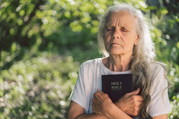 Die grauhaarige Großmutter hält die Bibel in den Händen.