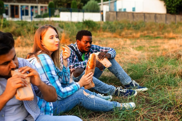 Die Gruppe junger, vielfältiger Menschen, die Fastfood in der Natur essen