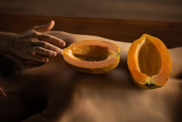 Die Hälfte der Papaya-Frucht auf dem Rücken der Frau. Duftendes tropisches Fruchtfleisch. Süße frische Papaya, rohes veganes Essen