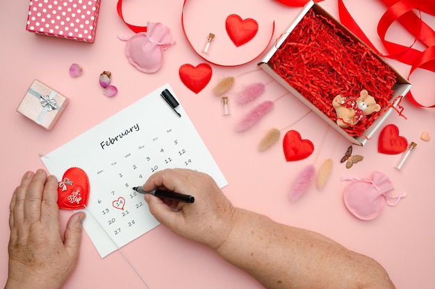 Die Hände älterer Frauen markieren das Datum des Valentinstags im Kalender mit einem roten Herz, das flach liegt