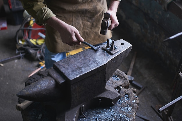 Die Hände bei der Herstellung von Kunsthandwerk aus Metall auf dem Amboss in der Werkstatt