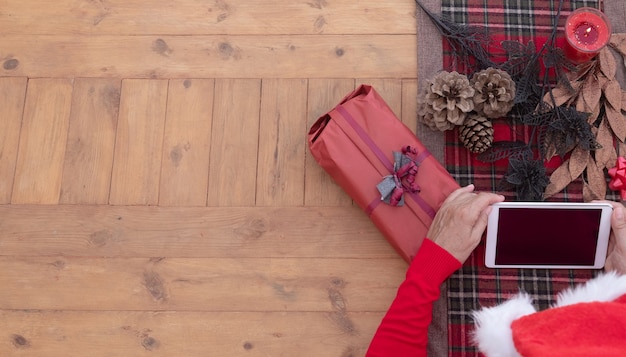 Die Hände der älteren Frau, die Technologie mit Tablette verwenden Holztisch verziert mit Weihnachten