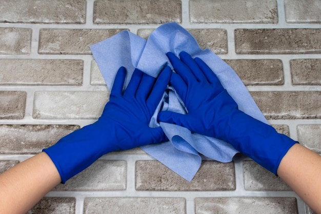 Die Hände der Arbeiter in Gummischutzhandschuhen mit einem Lappen, der die Oberfläche eines Tisches oder einer Wand in einer Badezimmerküche abwischt Das Konzept der Sauberkeit