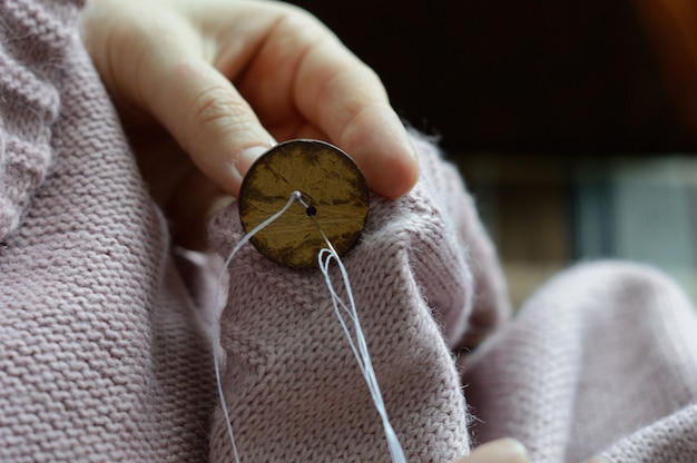 Die Hände der Arbeiterinnen nähen einen Holzknopf an eine Jacke. Nahaufnahme.