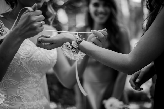 die hände der braut, die das hochzeitsarmband an der hand der brautjungfer bindenschwarzweißfoto